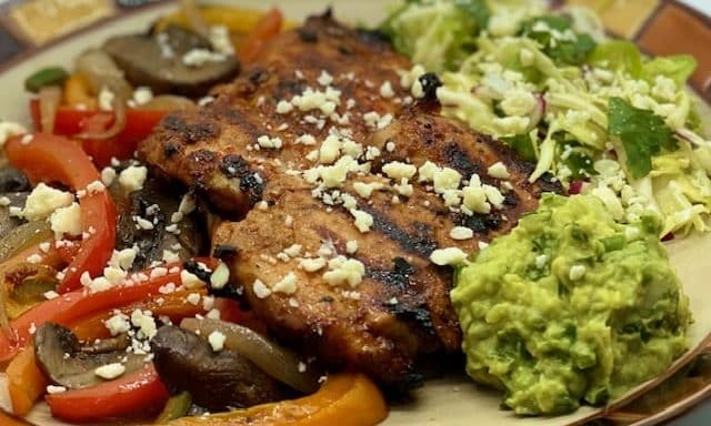 Grilled chicken served with mixed vegetables, guacamole, and crumbled cheese.