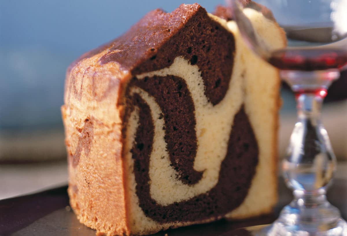 Close-up of a slice of tiger swirl cake with a chocolate and vanilla pattern, next to a wine glass.