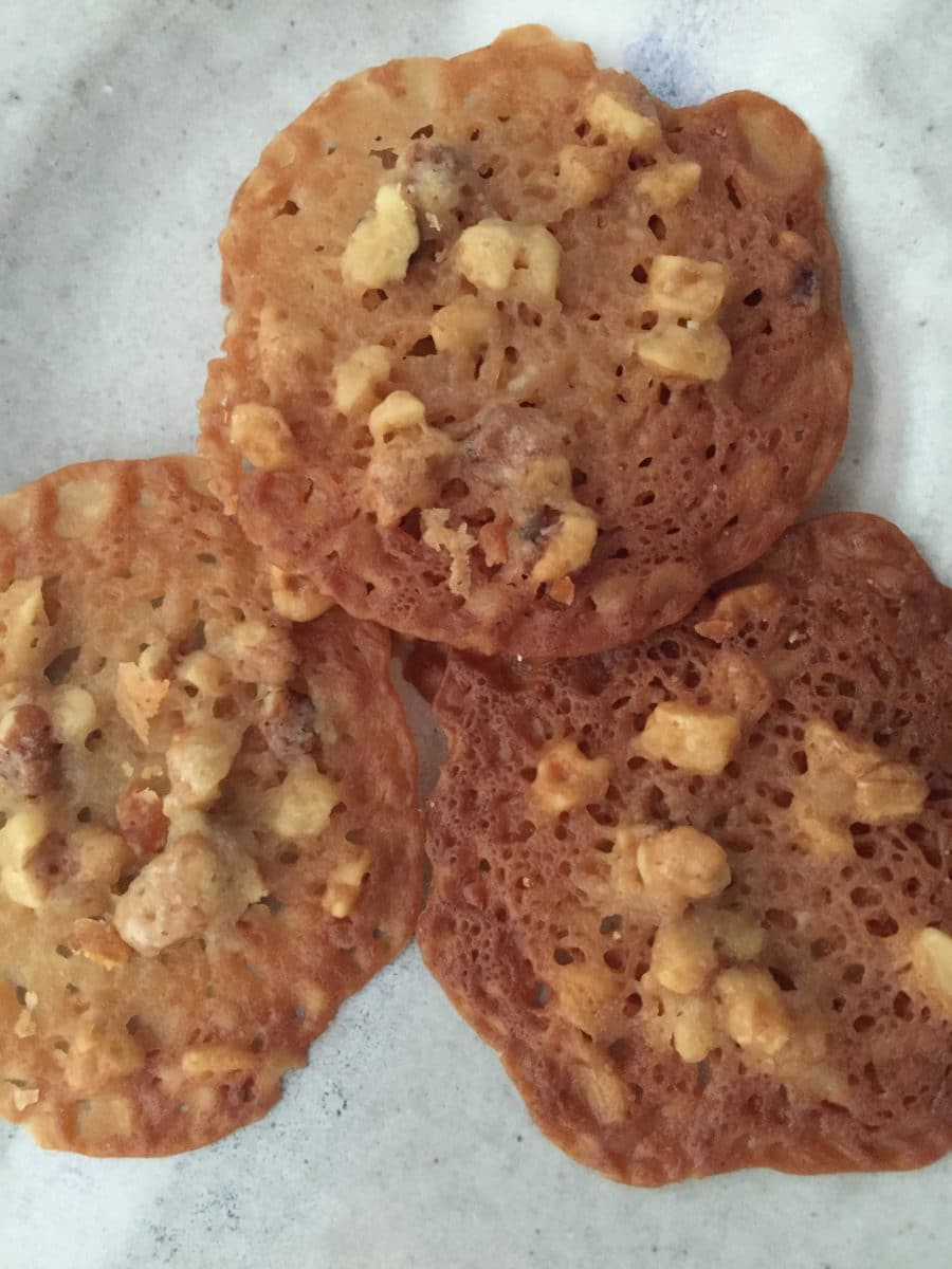 Round walnut lace cookies stacked on parchment paper.