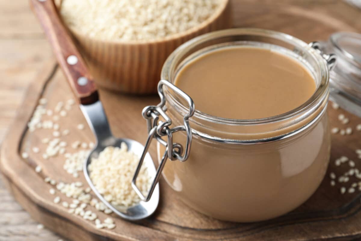 jar of tahini on table with sesame seeds