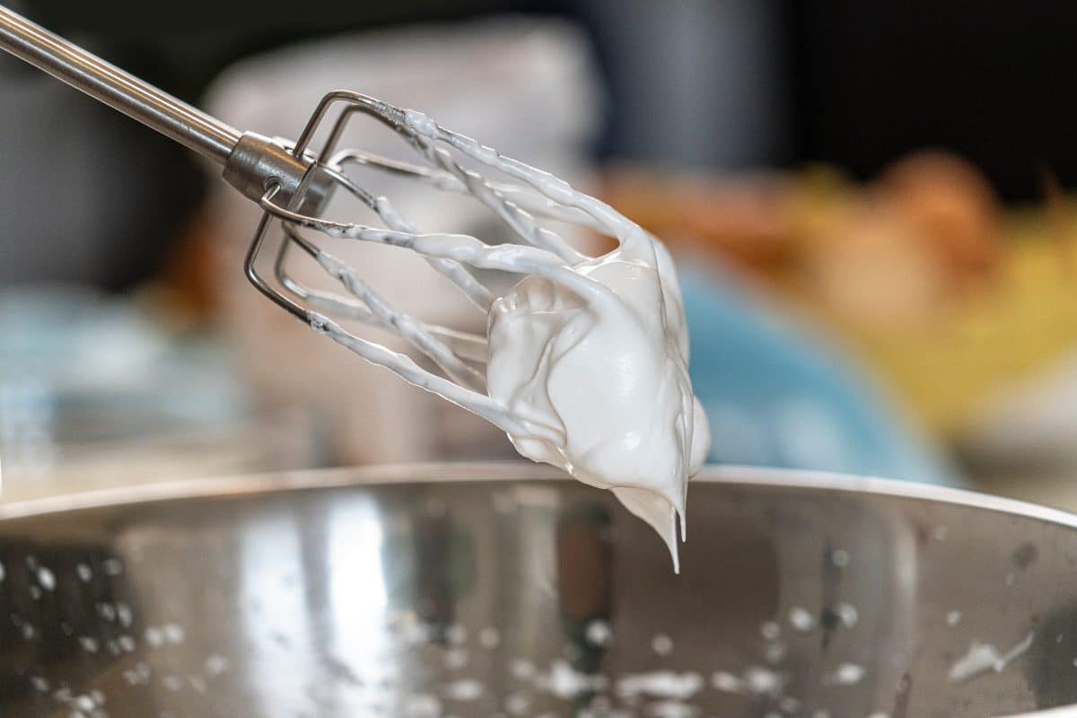 Whisk with whipped cream dripping off of it.