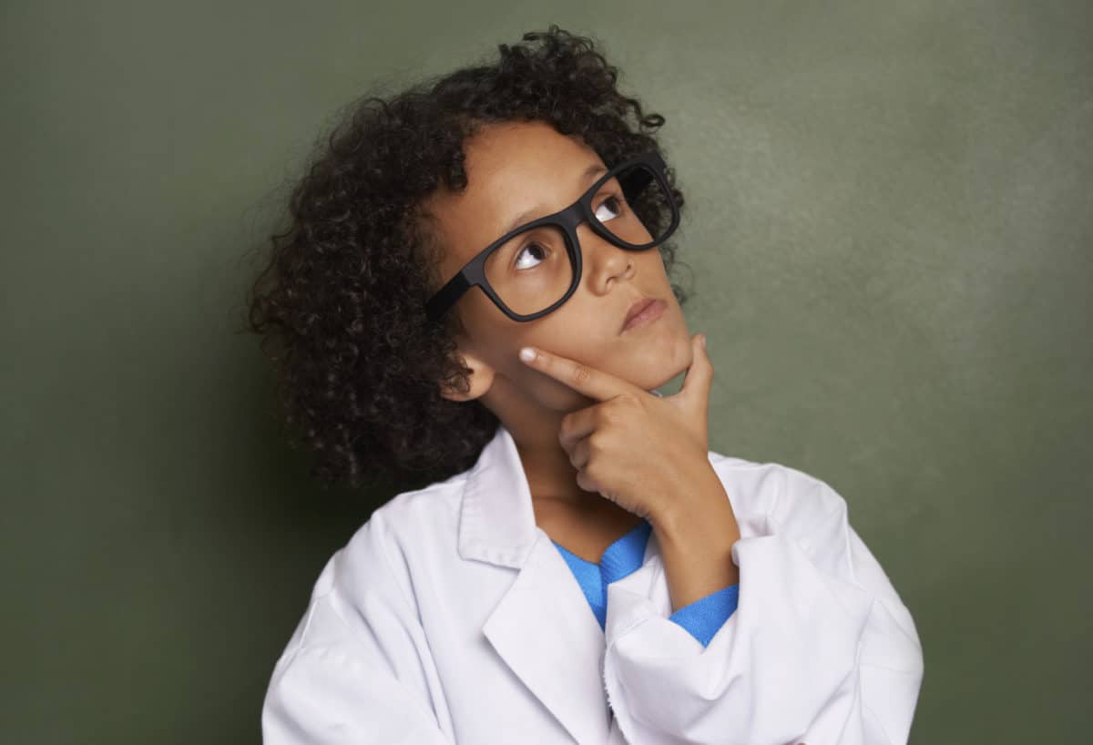 Young child with curly hair wearing glasses and a white coat, lost in thought
