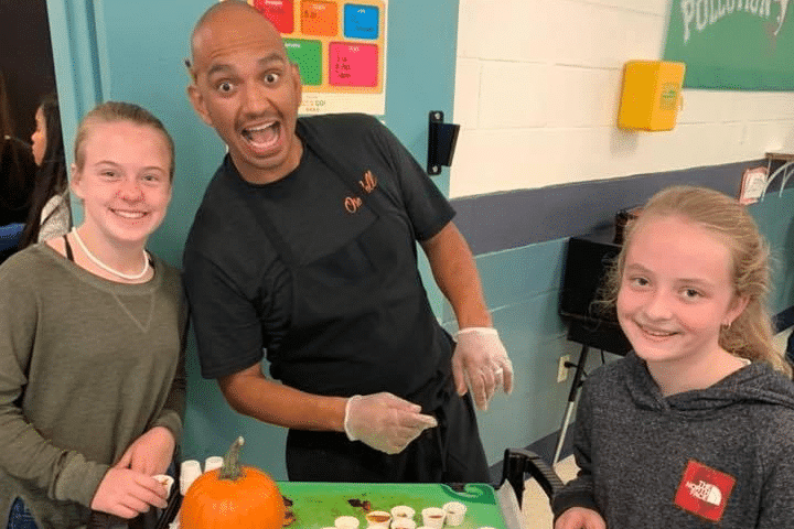 Chef Varga making a surprised face with two smiling young girls beside a table.