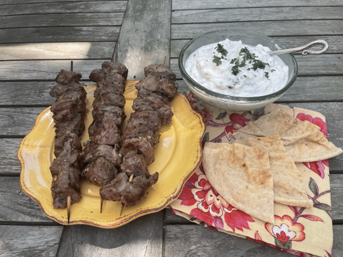 Lamb kebabs with yogurt sauce on a plate outdoors with ptia