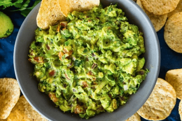 Fresh guacamole in a bowl surrounded by tortilla chips.