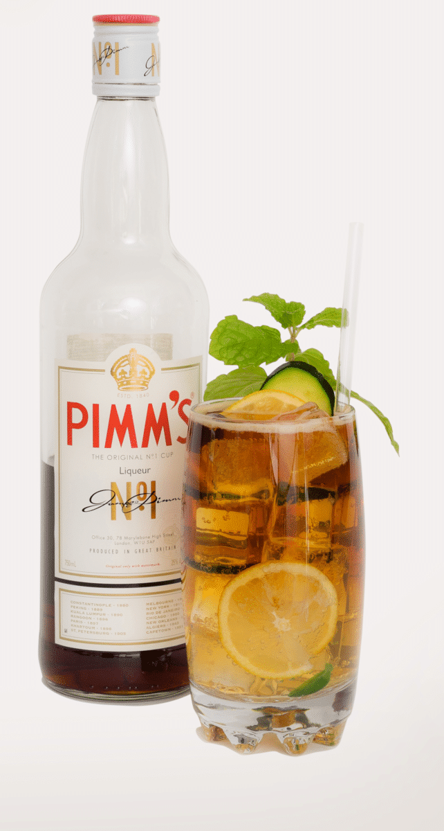 Close-up of a bottle of Pimm's next to a glass of Pimm's Cup, garnished with fresh ingredients.