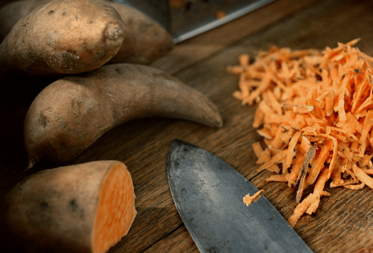 Close-up of sweet potato slices with a knife on a wooden background