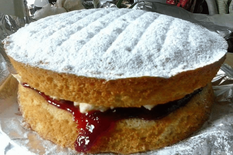 Layered Victoria sponge cake with jam filling and powdered sugar top.