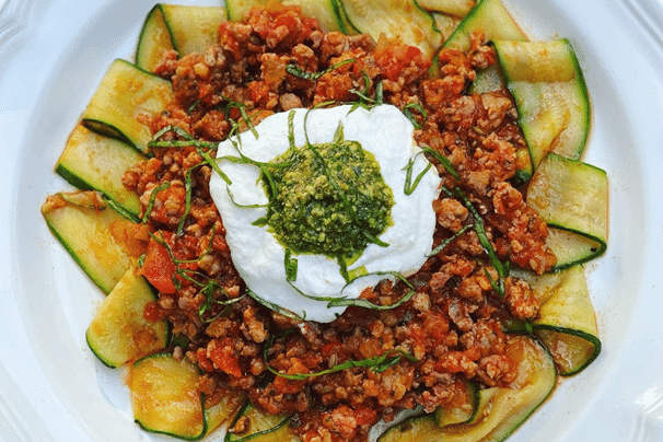 Dish of Zucchini Pappardelle Arrabbiata with a dollop of cream and pesto on top.